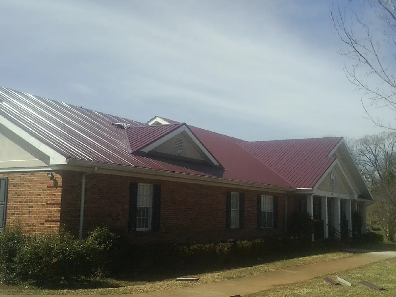 Red metal roof with gabled entries on a long brick building, from a Hail Damage Roof Repair job in Lacona