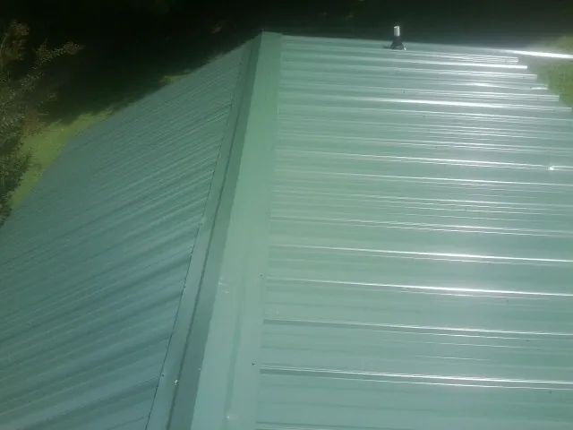 New green metal panels meeting at the ridge of a roof — Flat Roof Repair work by our crew in Lacona