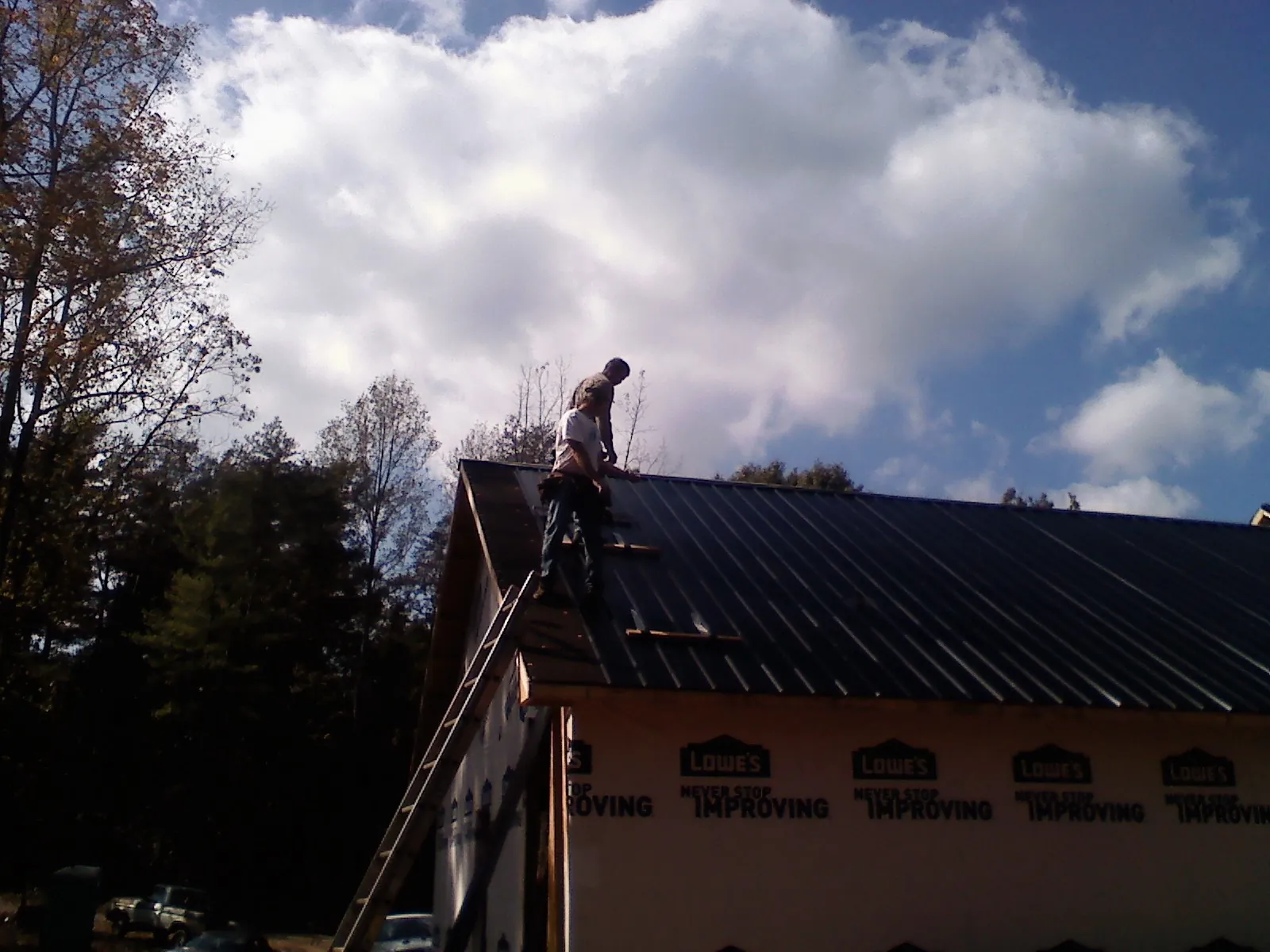 Roofer fastening dark metal panels high against a cloudy sky, from a Roof Inspection job in Lacona