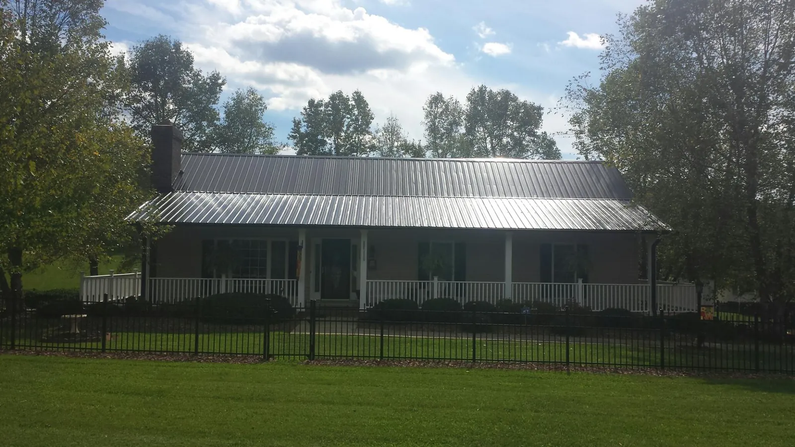 Gray metal roof on a brick ranch with a full width front porch — Gutter Guard Installation work by our crew in Lacona