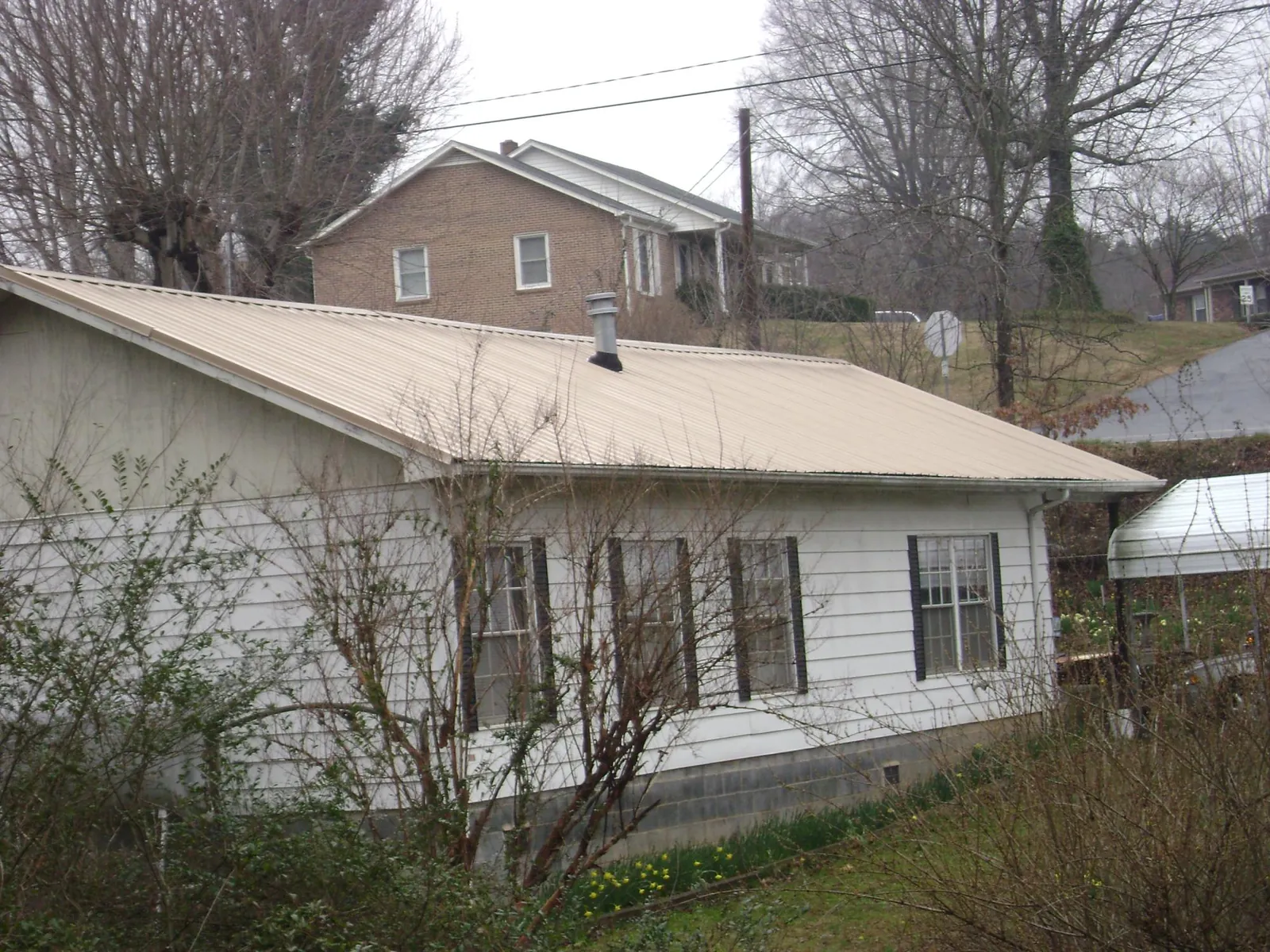 Tan metal roof on a white sided house set into a hillside — Commercial Roofing by Roofing Brothers in Lacona